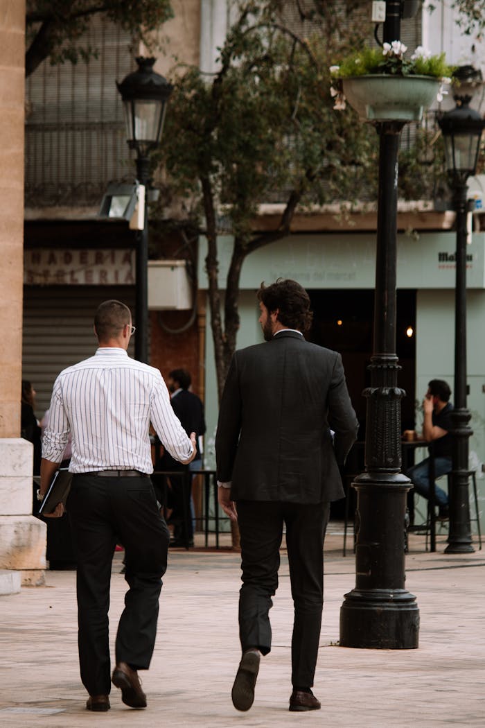 Two businessmen walking and talking in a city street, capturing a candid urban scene.